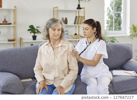 Doctor with stethoscope examining woman's breathing and heartbeat visiting senior patient at home Doctor with stethoscope examining woman's breathing and heartbeat visiting senior patient at home 127687227