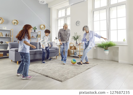 Active seniors loving elderly grandparents have fun playing ball with little children in living room Active seniors loving elderly grandparents have fun playing ball with little children in living room 127687235
