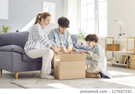 Unpacking carton box, mother, woman and teen, small kid son, family opening carton box, purchase 127687292