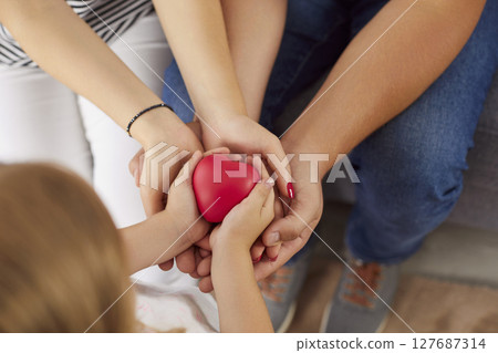 Top view of young family holding red heart in hands together sitting at home. 127687314