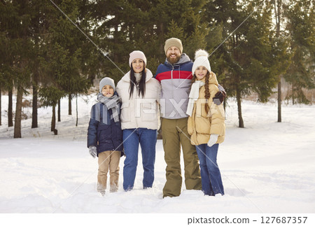 Portrait of happy smiling family of four with two kids walking in winter park and looking at camera 127687357