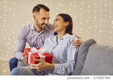 Joyful Couple Sharing Love and Surprises on the Sofa Joyful Couple Sharing Love and Surprises on the Sofa 127687360