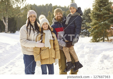 Portrait of happy family with two children posing together during walk in winter snowy park. Portrait of happy family with two children posing together during walk in winter snowy park. 127687363