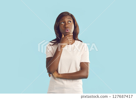 Portrait of young woman looking thoughtfully to the side isolated on studio blue background. 127687417