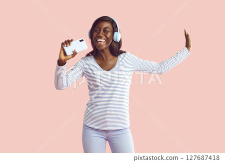 Happy young African woman in modern headphones listening to music on mobile phone Happy young African woman in modern headphones listening to music on mobile phone 127687418