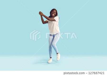 Young happy funny woman in casual clothes having fun isolated on studio blue background. Young happy funny woman in casual clothes having fun isolated on studio blue background. 127687421