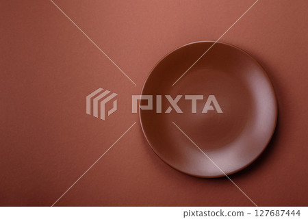 Empty ceramic plate on a monochrome brown background 127687444