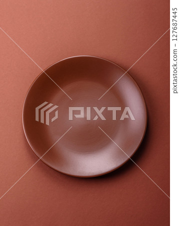 Empty ceramic plate on a monochrome brown background Empty ceramic plate on a monochrome brown background 127687445