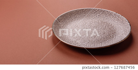 Empty ceramic plate on a monochrome brown background 127687456