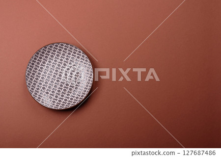 Empty ceramic plate on a monochrome brown background 127687486