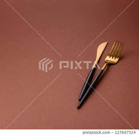 Knife and fork, cutlery on a brown dining table Knife and fork, cutlery on a brown dining table 127687524
