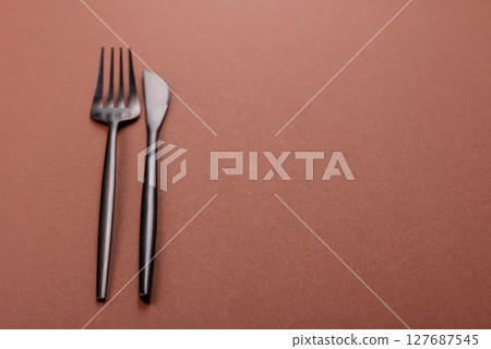 Knife and fork, cutlery on a brown dining table Knife and fork, cutlery on a brown dining table 127687545