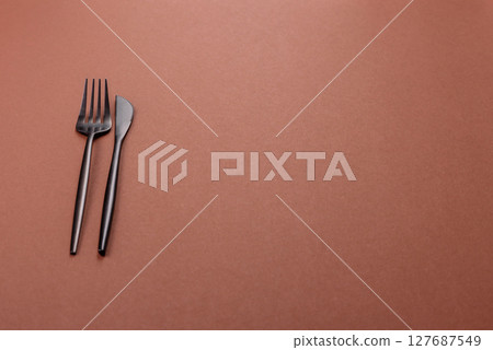 Knife and fork, cutlery on a brown dining table Knife and fork, cutlery on a brown dining table 127687549
