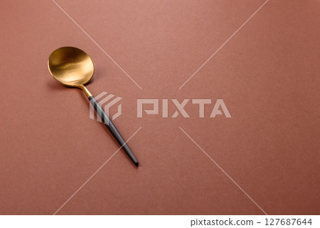 Empty metal spoon on a monochrome brown background Empty metal spoon on a monochrome brown background 127687644