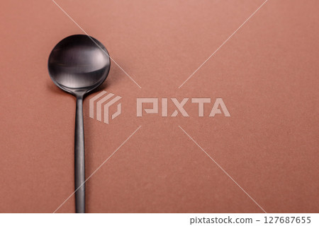 Empty metal spoon on a monochrome brown background 127687655