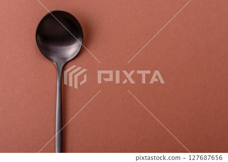 Empty metal spoon on a monochrome brown background 127687656