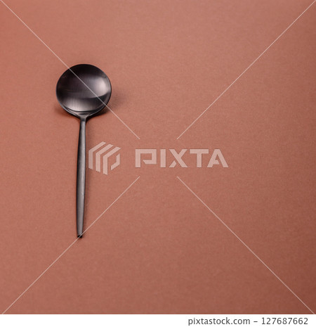 Empty metal spoon on a monochrome brown background 127687662