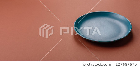 Empty ceramic plate on a monochrome brown background 127687679