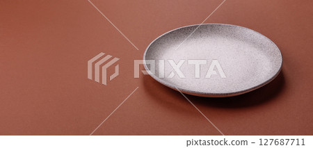 Empty ceramic plate on a monochrome brown background 127687711