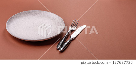 Empty ceramic plate on a monochrome brown background 127687723