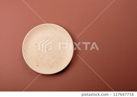 Empty ceramic plate on a monochrome brown background 127687738