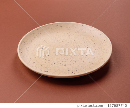 Empty ceramic plate on a monochrome brown background 127687740