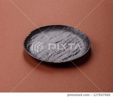 Empty ceramic plate on a monochrome brown background 127687880