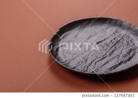 Empty ceramic plate on a monochrome brown background 127687881