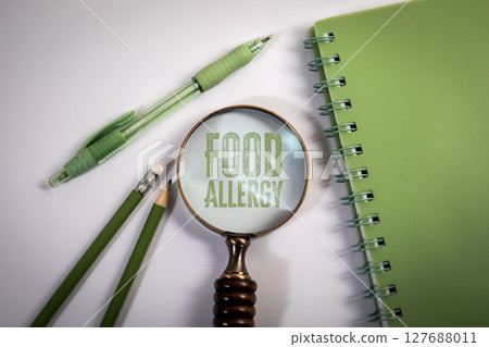Food Allergy Text Under Magnifying Glass with Green Stationery on White Background Food Allergy Text Under Magnifying Glass with Green Stationery on White Background 127688011