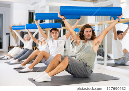 Group of people of different ages doing Pilates using rolled mats 127690682