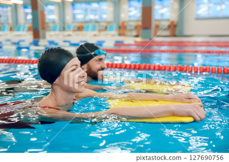 Young cute couple in swimming with boards in the pool 127690756