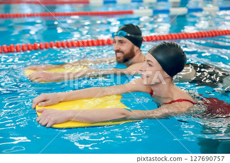 Young cute couple in swimming with boards in the pool 127690757