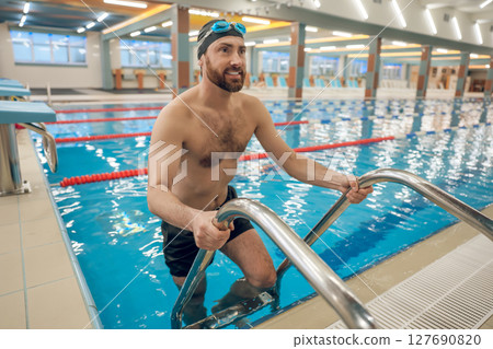 Man in swimming suit and swimming glassed on the ladder in the pool Man in swimming suit and swimming glassed on the ladder in the pool 127690820