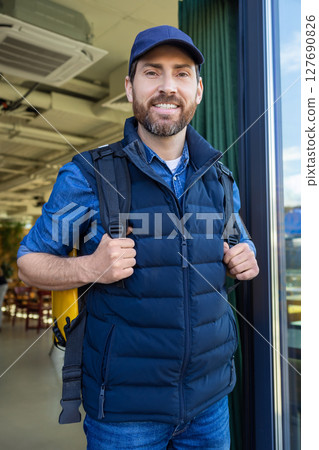 Delivery courier with yellow bag entering modern cafe 127690826