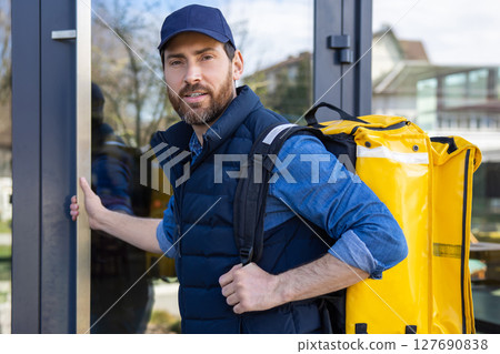 Delivery courier with yellow bag entering modern cafe 127690838