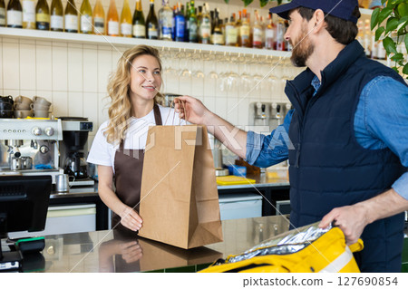 Barista passing delivery order to courier at cafe counter with bag 127690854