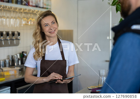 Waitress with tablet serving customer at cafe counter in modern interior 127690858