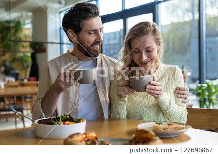 Couple sharing coffee and food at cozy restaurant with salad and pizza plates Couple sharing coffee and food at cozy restaurant with salad and pizza plates 127690862