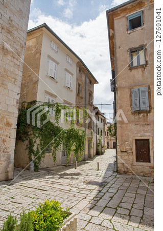 Picturesque narrow street with green plants in Porec, Croatia. 127691041