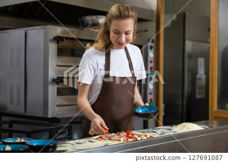 Woman adding toppings to pizza 127691087