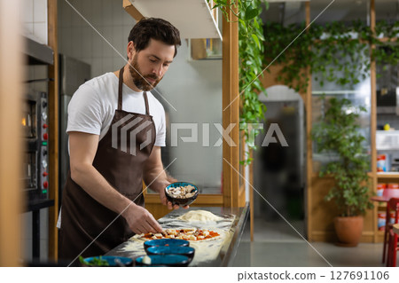 Man prepares pizza base in kitchen shaping dough carefully making meal Man prepares pizza base in kitchen shaping dough carefully making meal 127691106