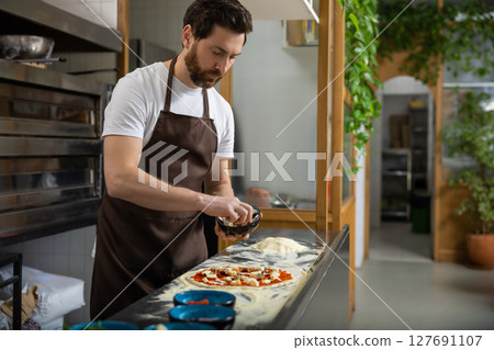 Man adds toppings pizza in kitchen arranging carefully creating food 127691107