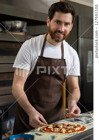 Man spreads sauce pizza in kitchen working neatly preparing meal 127691108