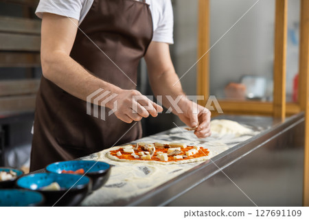 Man rolls dough in kitchen flattening carefully preparing pizza base Man rolls dough in kitchen flattening carefully preparing pizza base 127691109