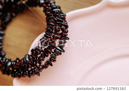 Dark red garnet chip bracelet on pink ceramic plate with wooden background 127691162