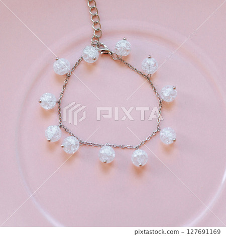 Silver chain bracelet with crackle glass beads on pink ceramic plate, top view, soft lighting Silver chain bracelet with crackle glass beads on pink ceramic plate, top view, soft lighting 127691169