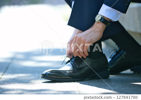 The feet of a young man in a suit tying the laces of his business shoes The feet of a young man in a suit tying the laces of his business shoes 127691780