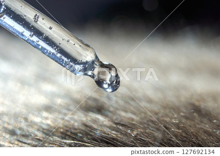 Close-up of pipette dropping liquid onto hair strands with dew drops in focus 127692134