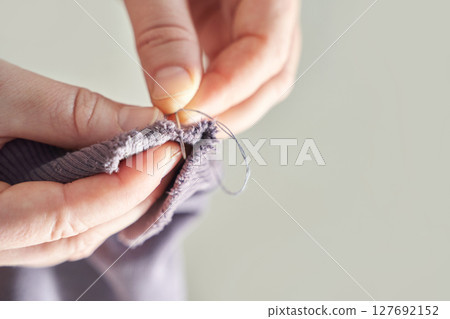 Close-up of hands sewing fabric with needle and thread for repairing and mending Close-up of hands sewing fabric with needle and thread for repairing and mending 127692152