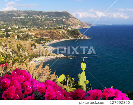 Stunning panoramic view of the blue sea from the top of Capo Vaticano mountain in Calabria, southern Italy. The foreground is adorned with red flowers and vibrant Mediterranean vegetation. Stunning panoramic view of the blue sea from the top of Capo Vaticano mountain in Calabria, southern Italy. The foreground is adorned with red flowers and vibrant Mediterranean vegetation. 127692800